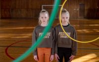 Twins stand indoors with hula hoops, promoting positive thoughts and teamwork.